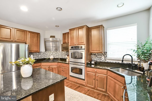 kitchen featuring appliances with stainless steel finishes, a sink, wood finished floors, decorative backsplash, and recessed lighting