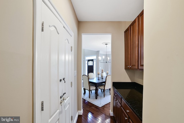 corridor featuring dark wood-style flooring, a chandelier, and baseboards