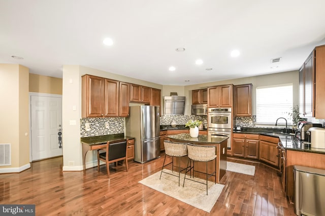 kitchen with appliances with stainless steel finishes, a sink, a center island, a kitchen bar, and tasteful backsplash