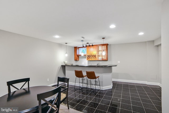 kitchen featuring brown cabinets, dark countertops, recessed lighting, a peninsula, and a breakfast bar area