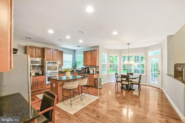 kitchen featuring appliances with stainless steel finishes, decorative backsplash, brown cabinetry, a chandelier, and a breakfast bar