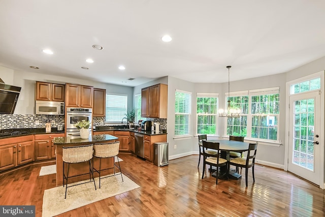 kitchen with stainless steel appliances, a sink, dark countertops, tasteful backsplash, and wood finished floors