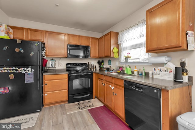 kitchen with black appliances, dark countertops, a sink, light wood finished floors, and brown cabinets