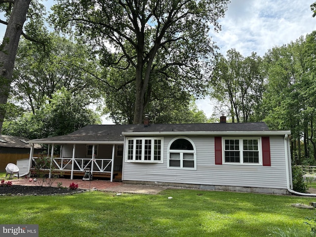 view of front of property with covered porch, a front lawn, and a chimney