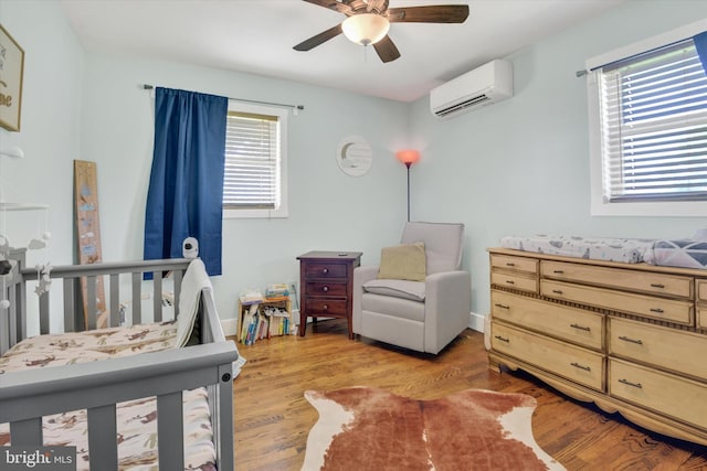 bedroom with a wall unit AC, light wood-type flooring, and a ceiling fan
