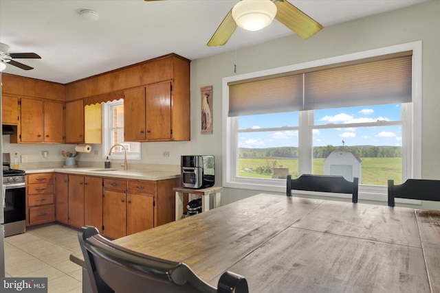 kitchen with ceiling fan, a sink, stainless steel gas stove, light countertops, and brown cabinetry