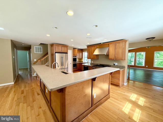 kitchen with stainless steel appliances, wall chimney range hood, brown cabinetry, baseboards, and recessed lighting
