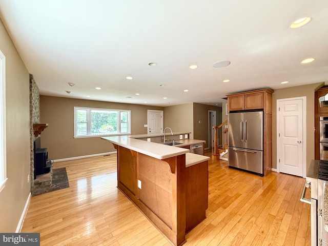 kitchen featuring appliances with stainless steel finishes, light wood-style flooring, a sink, brown cabinets, and a wood stove
