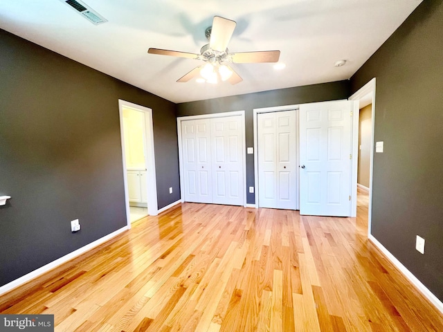 unfurnished bedroom featuring two closets, baseboards, light wood-style floors, and ensuite bath