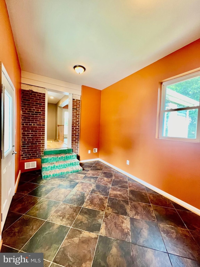 unfurnished room with baseboards and stone finish floors