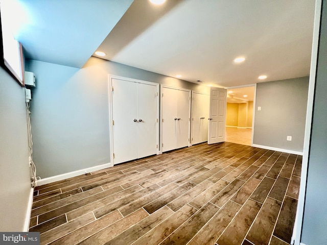unfurnished bedroom with wood finished floors, baseboards, recessed lighting, and two closets