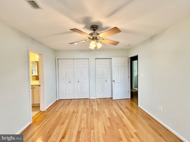 unfurnished bedroom featuring two closets, baseboards, light wood-style flooring, and a ceiling fan