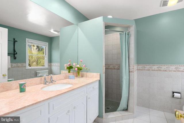 bathroom with tile walls, wainscoting, a stall shower, vanity, and tile patterned floors