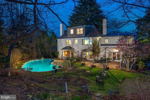 back of property with a chimney, an outdoor pool, and a yard