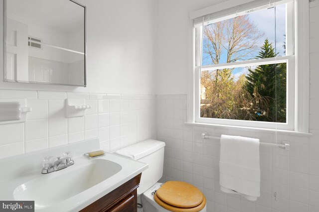 bathroom with toilet, vanity, and tile walls