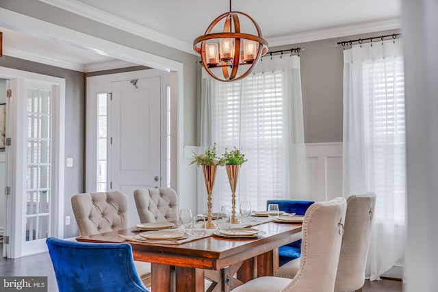 dining room with a chandelier, a wainscoted wall, crown molding, and wood finished floors