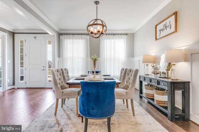 dining space featuring a chandelier, ornamental molding, wood finished floors, wainscoting, and a decorative wall