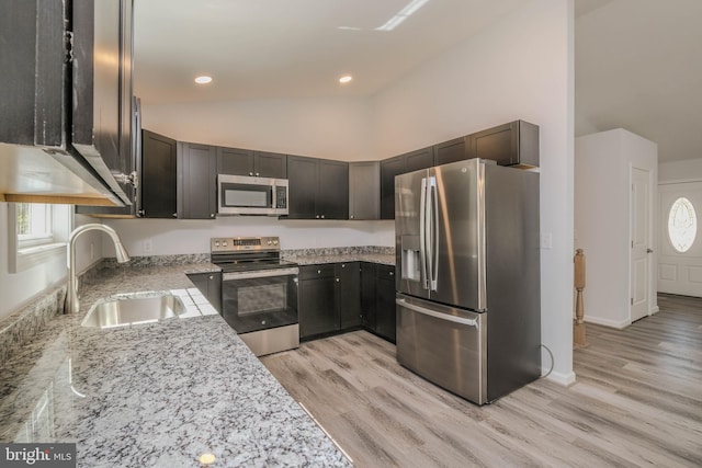 kitchen with appliances with stainless steel finishes, a sink, light wood-style flooring, light stone countertops, and healthy amount of natural light