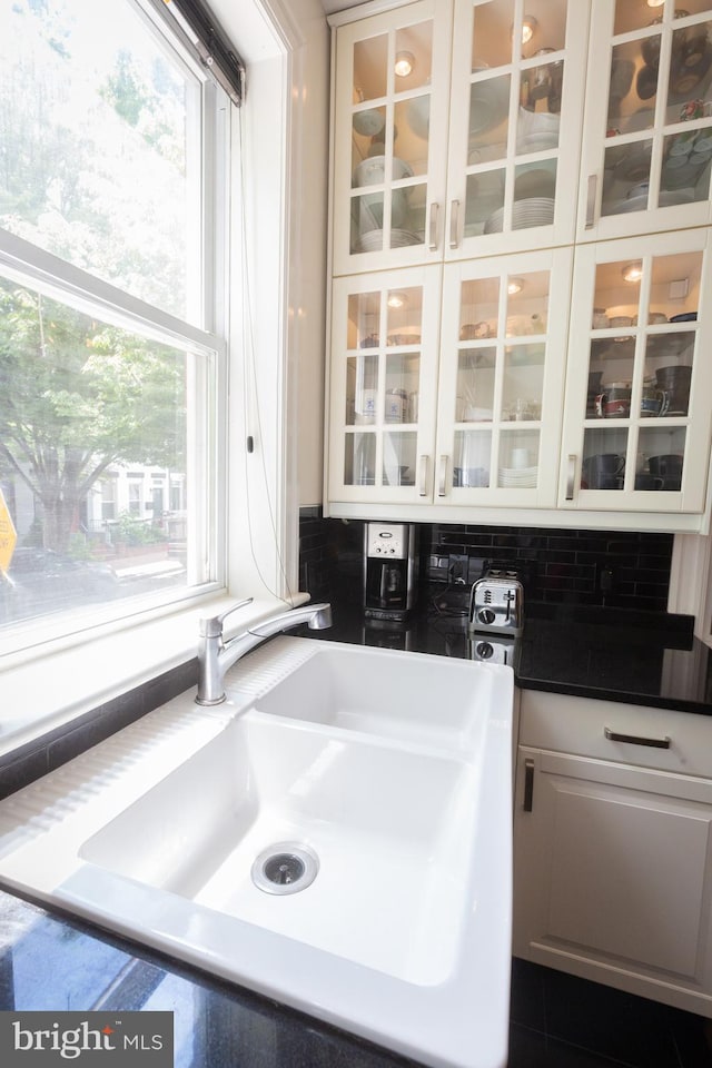 kitchen featuring a sink, glass insert cabinets, healthy amount of natural light, and dark countertops