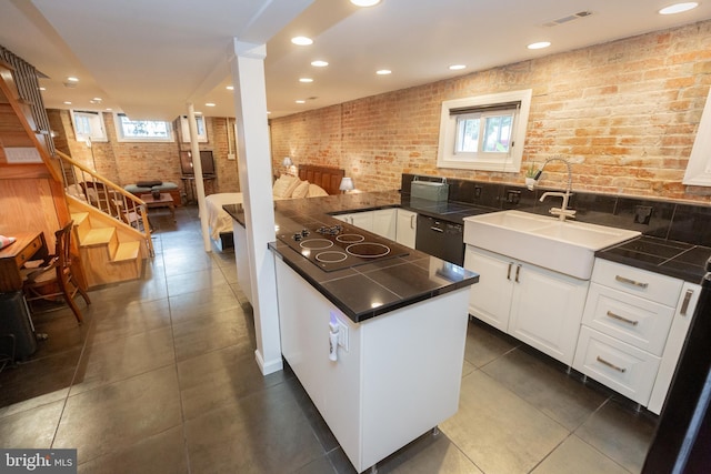 kitchen featuring a peninsula, a sink, black electric stovetop, brick wall, and white cabinets