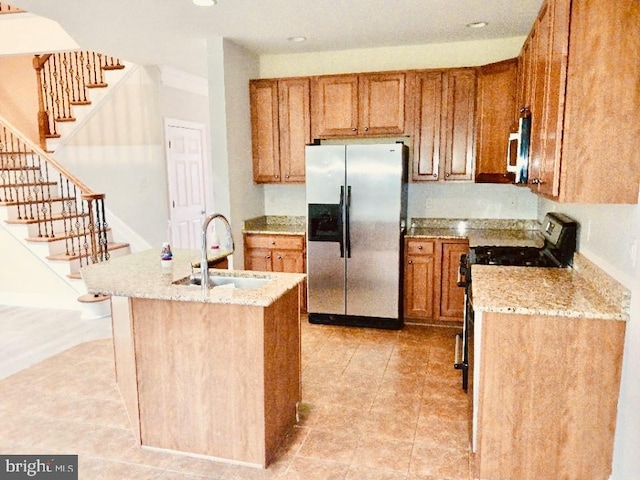 kitchen with appliances with stainless steel finishes, a sink, brown cabinetry, light stone counters, and light tile patterned floors