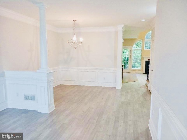 unfurnished dining area with a decorative wall, wainscoting, ornamental molding, ornate columns, and wood finished floors