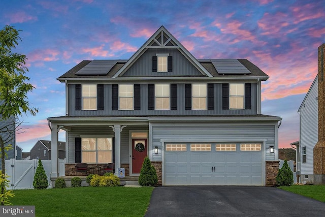 view of front of property featuring a porch, board and batten siding, roof mounted solar panels, and driveway