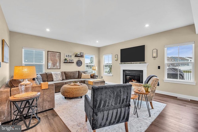 living room featuring a glass covered fireplace, wood finished floors, recessed lighting, and baseboards
