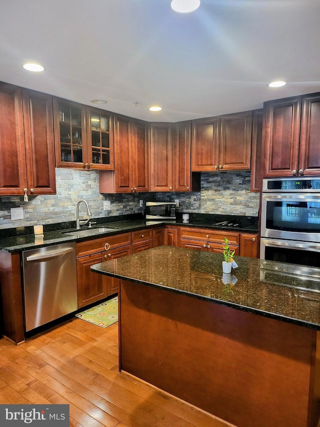 7100 Beltz Dr, District Heights, MD 20747 - kitchen with stainless steel appliances, a sink, light wood finished floors, decorative backsplash, and dark stone counters