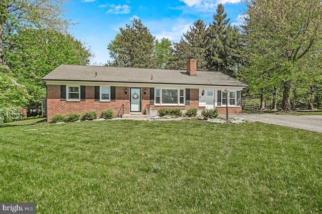 single story home featuring brick siding, a front lawn, a chimney, and asphalt driveway