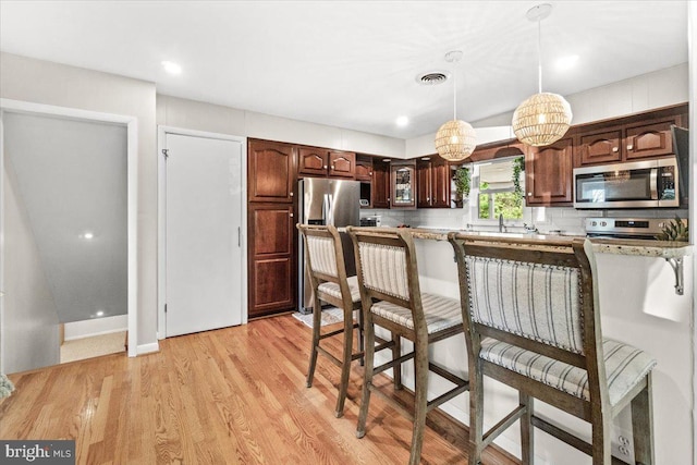 kitchen with appliances with stainless steel finishes, a breakfast bar, decorative light fixtures, and light wood-style floors