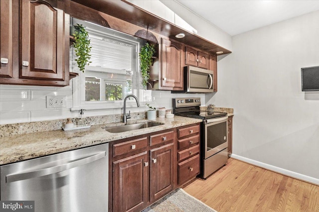 kitchen featuring appliances with stainless steel finishes, a sink, light wood finished floors, light stone counters, and baseboards