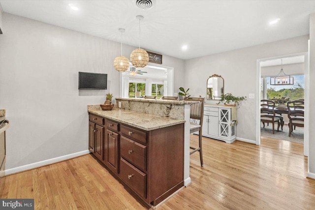 kitchen featuring a kitchen breakfast bar, a peninsula, a chandelier, baseboards, and light wood-type flooring