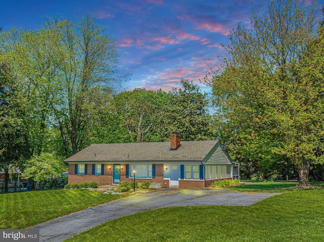 single story home with asphalt driveway, brick siding, a chimney, a front yard, and roof with shingles