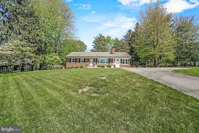 ranch-style house with brick siding, a chimney, a front lawn, and driveway