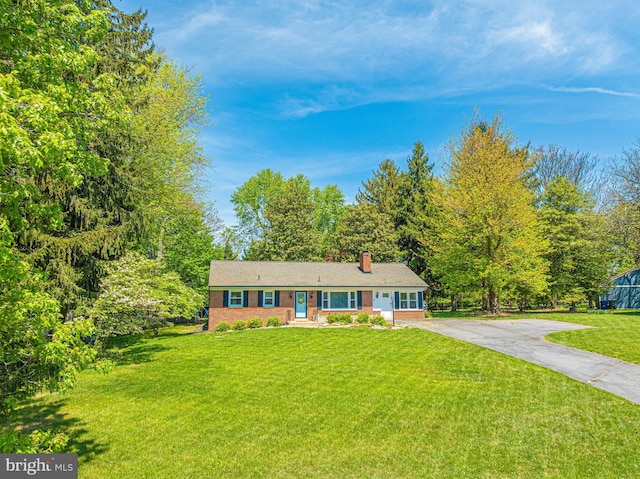 view of front of property featuring a chimney, concrete driveway, brick siding, and a front lawn