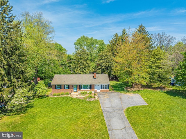 ranch-style house with driveway, a front lawn, a chimney, and a forest view