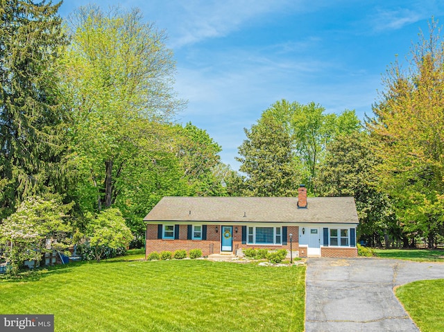 view of front of home with brick siding, a chimney, a front lawn, asphalt driveway, and a shingled roof