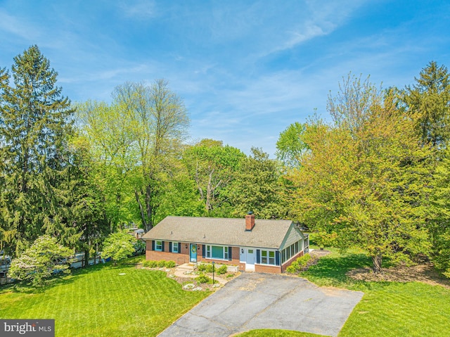 ranch-style house with a chimney, a front yard, asphalt driveway, and brick siding