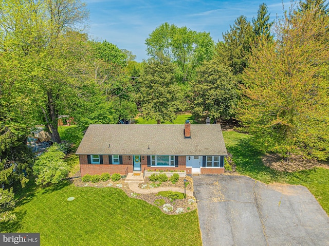 view of front of house with brick siding, a chimney, a front lawn, and asphalt driveway