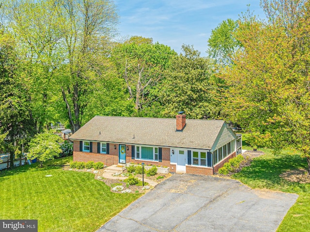 ranch-style home featuring brick siding, a chimney, a front lawn, a shingled roof, and asphalt driveway