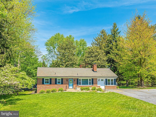 ranch-style home featuring brick siding, a chimney, a front yard, and driveway