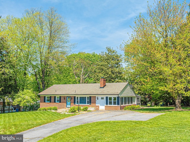 ranch-style house featuring brick siding, asphalt driveway, a chimney, and a front yard