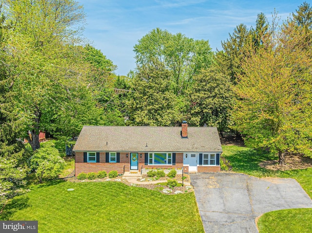 view of front of home featuring brick siding, a chimney, a front lawn, and driveway