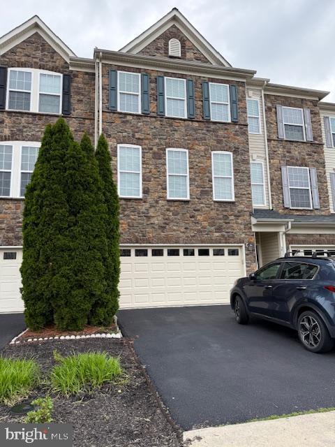 view of property with asphalt driveway, a garage, and stone siding