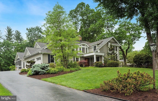 shingle-style home featuring a front lawn, an attached garage, a chimney, and asphalt driveway