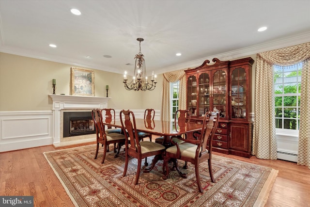 dining area featuring a baseboard radiator, healthy amount of natural light, light wood-style flooring, wainscoting, and ornamental molding