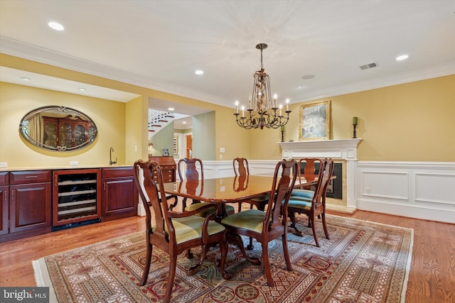 dining area with wine cooler, wainscoting, light wood-style floors, crown molding, and a chandelier