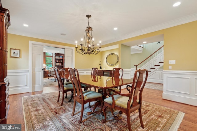 dining room with a wainscoted wall, light wood-style floors, stairs, a decorative wall, and crown molding