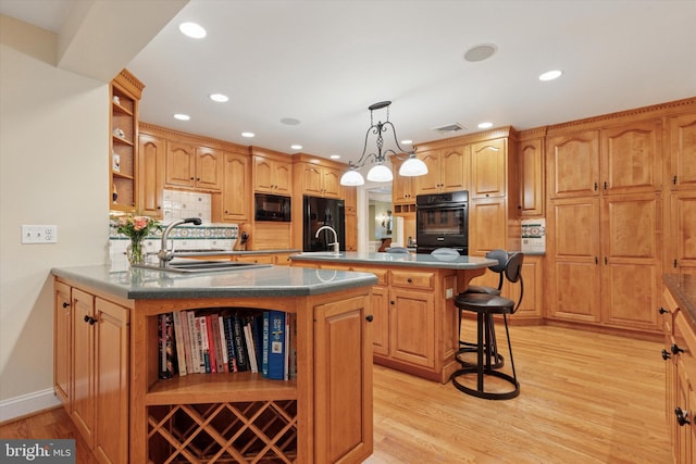 kitchen featuring open shelves, black appliances, a breakfast bar area, a kitchen island with sink, and light wood-style flooring